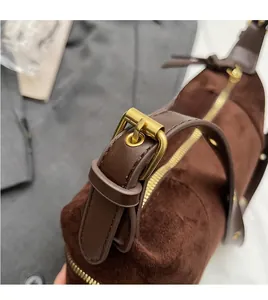Close-up of brown suede bag featuring an adjustable shoulder strap and gold metal buckle