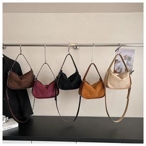 Detail view of five assorted suede crossbody crescent bags hanging in a row on a rack