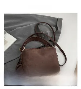 Detail of brown suede crossbody bag featuring fringed sides and woven handles