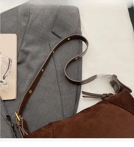 Detail of brown suede tote bag featuring deep brown leather strap with gold eyelets