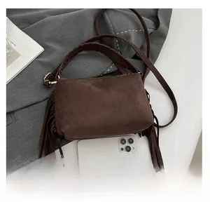 Macro shot of dark brown suede bag with fringe details and braided handle next to an iPhone
