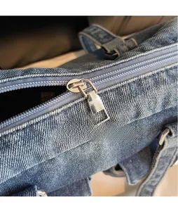 Detail of silver smooth metal zipper pull on blue denim underarm bag texture