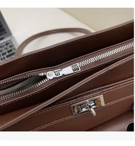 Detail of silver metal zipper and turn-lock on dark brown textured leather tote bag