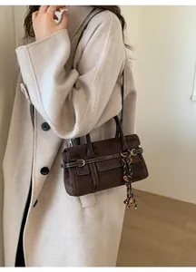 Detail view of dark brown matte leather handbag with white stitching and woven charm