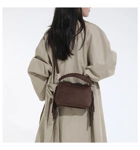 Detail of dark brown suede bag with long side tassels and woven handle texture