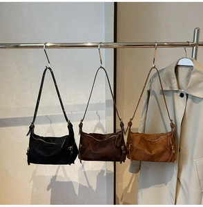Three suede crescent shoulder bags in black, dark coffee, and caramel brown on display