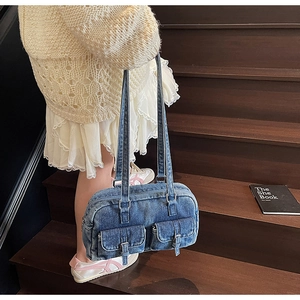 Detail of blue denim shoulder bag with utility pockets and slim straps on a model