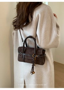Détail du sac à main rétro en daim marron avec coutures blanches et pompon à clochette