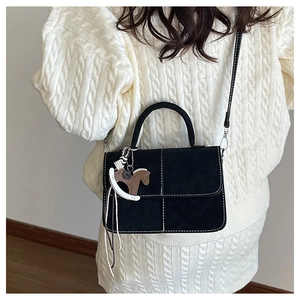 Detail of black suede handbag with contrast stitching and horse charm on a white sweater
