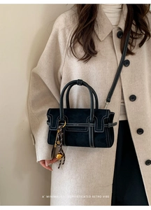 Detail of black crossbody bag with white contrast stitching and gold bell charm
