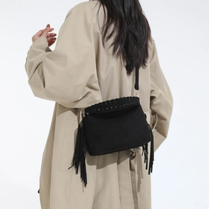 Vintage black fringed crossbody bag with woven details shown on model in a beige coat