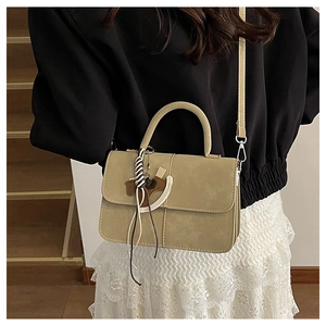 Detail of khaki square handbag with horse charm and tassel strap shown in lifestyle setting