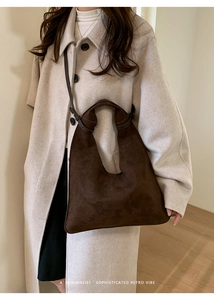 Detail view of dark brown faux suede tote bag on cream coat showing retro minimalist style