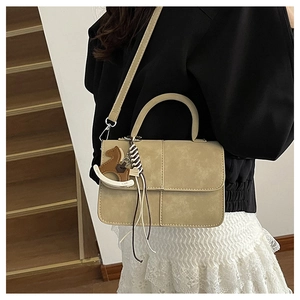 Model wearing a beige rectangular crossbody bag with a horse pendant on a staircase
