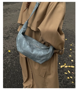 Detail of grey-blue dumpling crossbody bag in matte texture with autumn trench coat