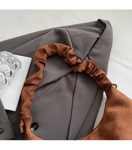 Detail of soft brown suede hobo bag with pleated shoulder strap on grey blazer