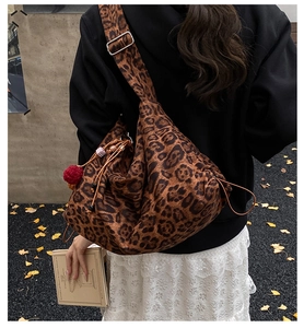 Outdoor view of a leopard print canvas tote bag with drawstring and red pompom charm