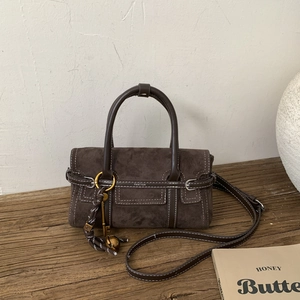 Detail of dark brown suede handbag with white stitching and decorative charms on wood