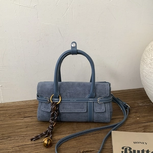 Blue suede mini bag featuring cylindrical handles and decorative woven bell charm detail