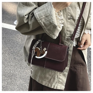 Close-up of retro burgundy shoulder bag featuring contrast stitching and wooden horse charm