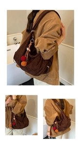 Close-up of a deep brown suede tote bag with soft pleats and decorative pompom charm