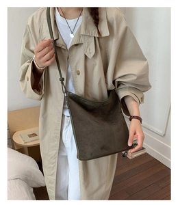 Close-up of olive green suede crossbody bag styled with a beige trench coat for a city look