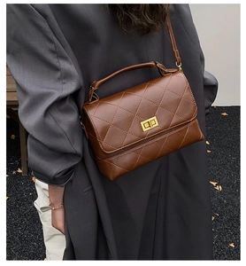 Détail d'un sac bandoulière marron matelassé avec fermoir doré porté par un modèle