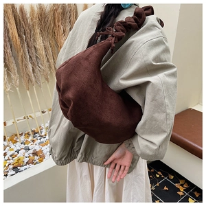 Detail of soft brown suede hobo bag with pleated shoulder strap worn by a model