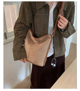 Detail of tan suede tote bag with leather trim worn by a model in a natural setting