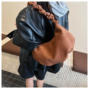 Detail of a brown suede dumpling bag with a large pleated strap shown on a model