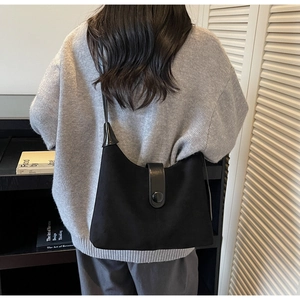 Minimalist black suede hobo bag with leather buckle detail worn by a model on shoulder