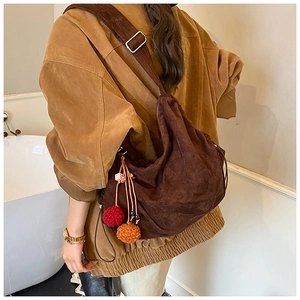 Detail of dark brown suede tote bag featuring colorful pompom charms and adjustable strap