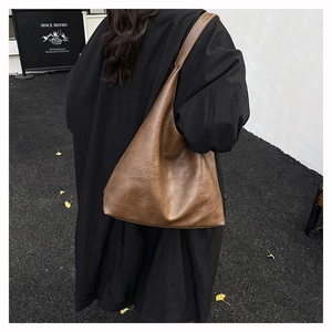 Detail of a large brown vintage faux leather tote bag worn with a black winter coat