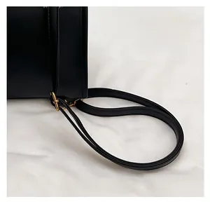 Detail of black leather bag showing fine stitching, slim shoulder strap, and gold metal hook