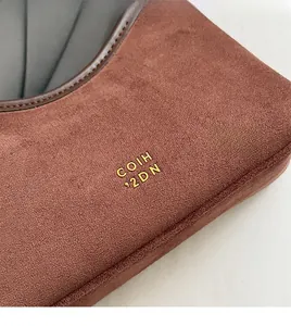 Detailaufnahme von braunem Wildleder mit goldener Logo-Prägung an der Eimertasche