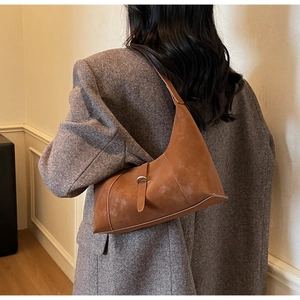 Close-up of brown suede crescent hobo bag with vintage metal buckle on a grey blazer