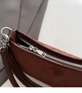 Detail eines silbernen Metallreißverschlusses und rotbraunem Wildlederimitat an Tasche