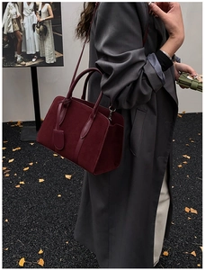 Détail du sac Boston en cuir bordeaux mat porté avec un long manteau en laine gris