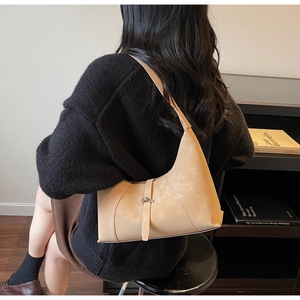 Detail of minimalist beige shoulder bag showing matte texture and unique buckle closure