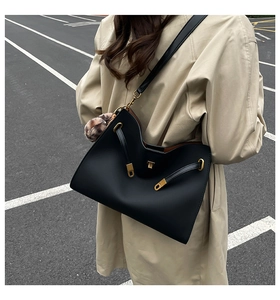 Detail of black matte tote bag with gold twist lock, adjustable strap and leopard pompom
