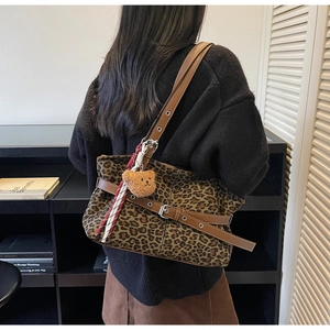Detail of leopard print tote bag featuring brown leather straps and a plush bear charm