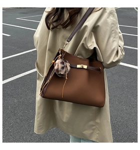 Close-up of brown tote bag with gold metal buckle and leopard print pom-pom charm