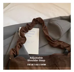 Detail shot of the adjustable gathered shoulder strap on a brown suede crossbody bag