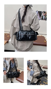 Close-up of black PU leather multi-pocket shoulder bag with silver zippers in city setting