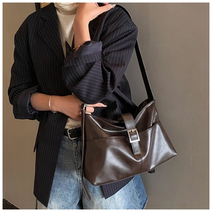 Close-up of a stylish dark brown faux leather tote bag worn with a striped business blazer