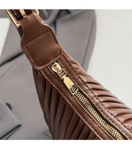 Close-up of golden metal zipper and quilted pleat texture on brown leather bag