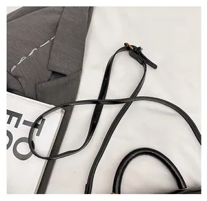 Detail view of the adjustable black leather shoulder strap and top handle of the bag