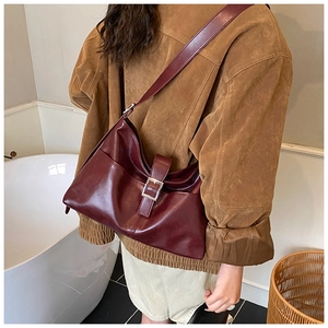 Detail of burgundy leather shoulder bag showing the large metal buckle and premium texture