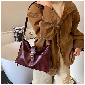 Detail of burgundy glossy shoulder bag featuring silver buckle and retro side pockets