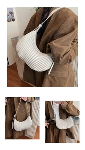 Close-up of a white pleated croissant bag with a sleek metal zipper and curved handle